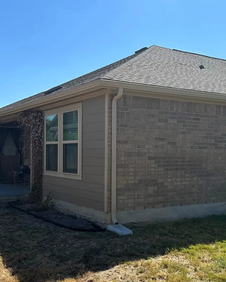 A PSG job: new gutter and a tan downspout at the corner of a brick and siding house
